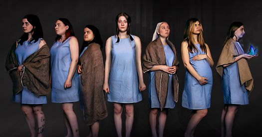 Sju kvinnor i blå klänningar framför en vägg